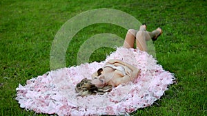 Young blonde girl in pink elegant dress lying on the green lawn