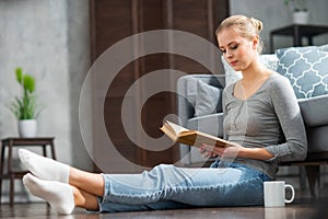 Young blonde girl is reading a book or a textbook. A beautiful woman is resting and relaxing at home.