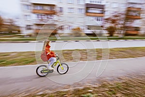 Young blonde girl in red jacket riding bike