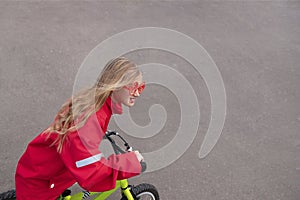 Young blonde girl in red jacket riding bike