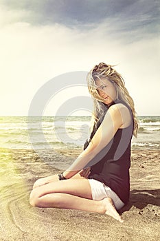 Young blonde girl relaxing on the beach sand. Wind in her blonde hair