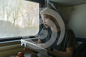 A young blonde girl rides on a train and reads a book. Education, training and travel. Close-up