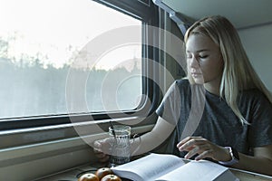 A young blonde girl rides on a train and reads a book. Education, training and travel. Close-up