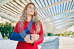 Young blonde girl with serious expression injuried with arm sling standing at the park