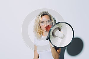 Young blonde girl shouting by megaphone isolated on white background