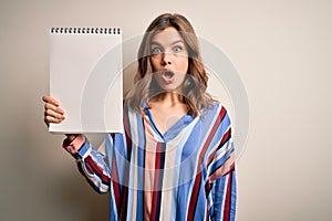 Young blonde girl showing white space paper on notebook over isolated background scared in shock with a surprise face, afraid and