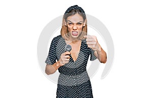 Young blonde girl singing song using microphone annoyed and frustrated shouting with anger, yelling crazy with anger and hand