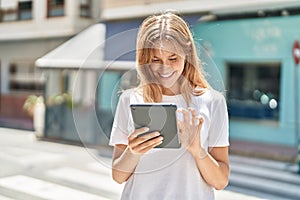 Young blonde girl smiling confident using touchpad at street