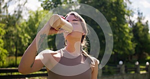 A young blonde girl in a special summer sports uniform drinks water from a yellow bottle against the backdrop of a green