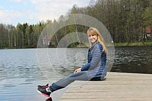 A young blonde girl is sitting on the shore of the lake