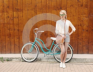 Young blonde girl is standing near the vintage green bicycle with brown vintage bag in green sunglasses, warm, tonning