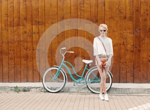 Young blonde girl is standing near the vintage green bicycle with brown vintage bag in orange sunglasses, warm, tonning