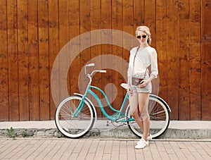 Young blonde girl is standing near the vintage green bicycle with brown vintage Cameras in orange sunglasses., warm, tonning