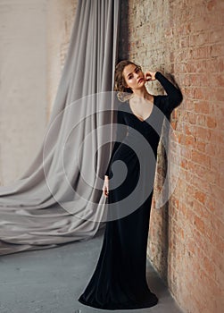 A young blonde girl in a strict, discreet, modest, elegant, long black dress. Delicate natural make-up. Beautiful