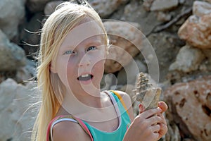 Young blonde girl surprised and holding a seashell