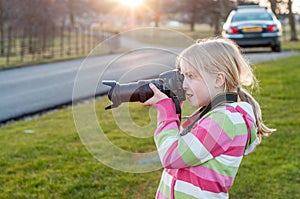 A young blonde girl using a camera with a large zoom lens