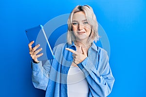 Young blonde girl using touchpad device smiling happy pointing with hand and finger