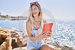 Young blonde girl using touchpad sitting on the rock at the beach