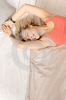 Young blonde girl waking up, looking at the side, smiling. Beautiful woman in a good mood lies on the bed, stretching