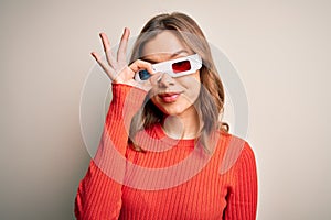 Young blonde girl wearing 3d cinema glasses over isolated background doing ok gesture with hand smiling, eye looking through