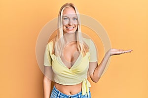 Young blonde girl wearing casual clothes smiling cheerful presenting and pointing with palm of hand looking at the camera