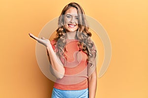 Young blonde girl wearing casual clothes smiling cheerful presenting and pointing with palm of hand looking at the camera