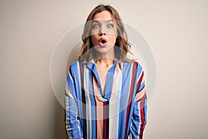 Young blonde girl wearing colorful striped shirt over isolated background afraid and shocked with surprise expression, fear and