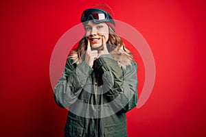 Young blonde girl wearing ski glasses and winter coat for ski weather over red background Smiling with open mouth, fingers