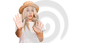 Young blonde girl wearing summer hat afraid and terrified with fear expression stop gesture with hands, shouting in shock