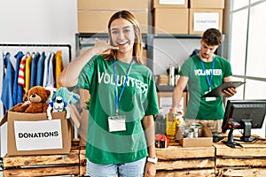 Young blonde girl wearing volunteer t shirt at donation stand smiling doing phone gesture with hand and fingers like talking on