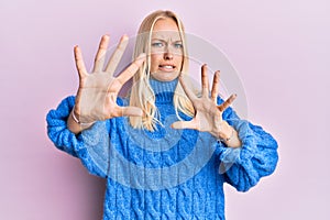 Young blonde girl wearing wool winter sweater afraid and terrified with fear expression stop gesture with hands, shouting in shock