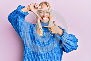 Young blonde girl wearing wool winter sweater smiling making frame with hands and fingers with happy face