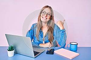 Young blonde girl working at the office drinking a cup of coffee smiling happy and positive, thumb up doing excellent and approval