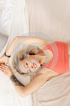 Young blonde-hair girl waking up, smiling, looking at the camera. Beautiful woman in a good mood lies on the bed
