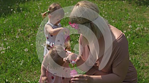 Young blonde hippie mother having quality time with her baby girls at a park blowing soap bubbles - Daughters wear