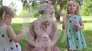Young blonde hippie mother having quality time with her baby girls at a park blowing soap bubbles - Daughters wear