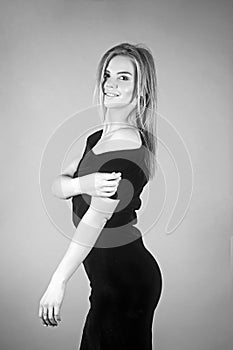 Young blonde lady in black dress posing on grey background.