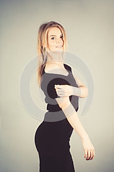 Young blonde lady in black dress posing on grey background.