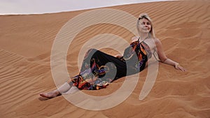 A young blonde lies on a pesce in the desert. Woman in the dunes.
