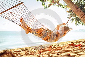 Young blonde longhaired woman relaxing in hammock hinged between palm trees on the sand beach