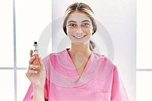 Young blonde nurse woman holding electronic cigarette looking positive and happy standing and smiling with a confident smile