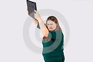 Young blonde overwight businesswoman in green dress over gray background, frustrated large woman holding pc computer up