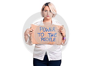 Young blonde plus size woman holding power to the people banner thinking attitude and sober expression looking self confident