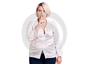 Young blonde plus size woman wearing casual shirt asking to be quiet with finger on lips
