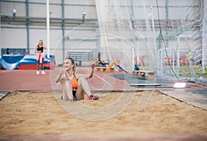 Young blonde smiling women performing a long jump in the sports arena. Sitting in the sand