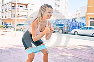 Young blonde sporty girl smiling happy using elastic band to do sport at street of city