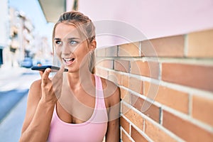 Young blonde sporty girl talking on the smartphone leaning on the wall at street of city