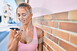 Young blonde sporty girl talking on the smartphone leaning on the wall at street of city