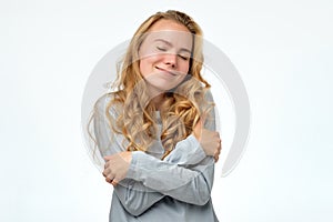 Young blonde teenager girl hugging oneself being happy and smiling confident