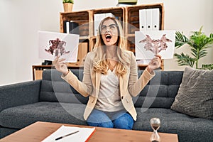 Young blonde therapist woman holding rorschach test angry and mad screaming frustrated and furious, shouting with anger looking up